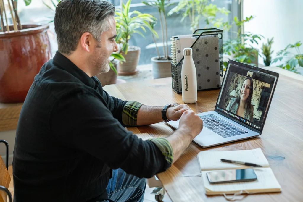 A bearded man in front of a laptop on a video call