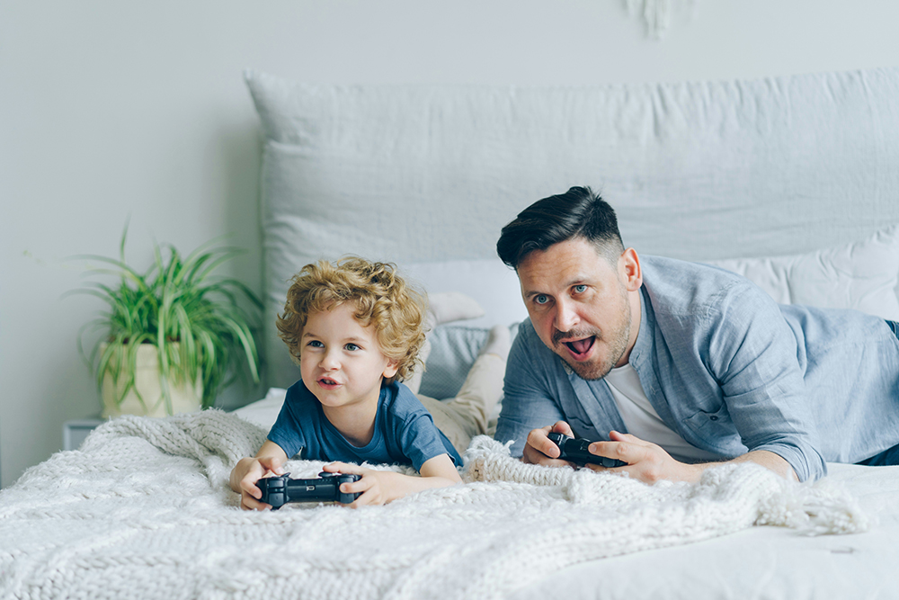 A dad playing a games console with their child.